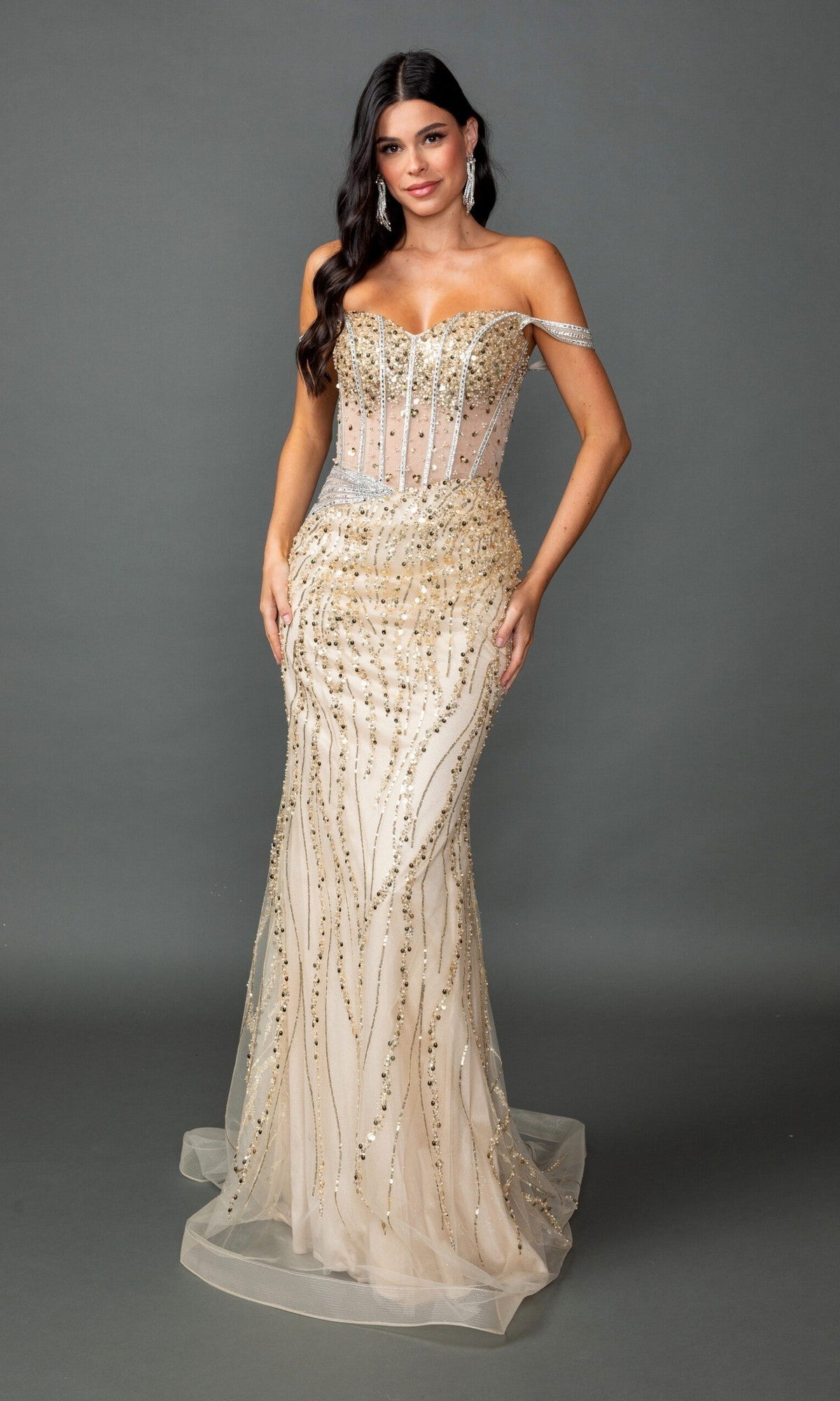 A woman wearing the Long Prom Dress: Dancing Queen 4598 in Champagne—a strapless, fitted, floor-length gown adorned with gold sequins and beads and featuring a sheer corset bodice—stands against a plain gray background.